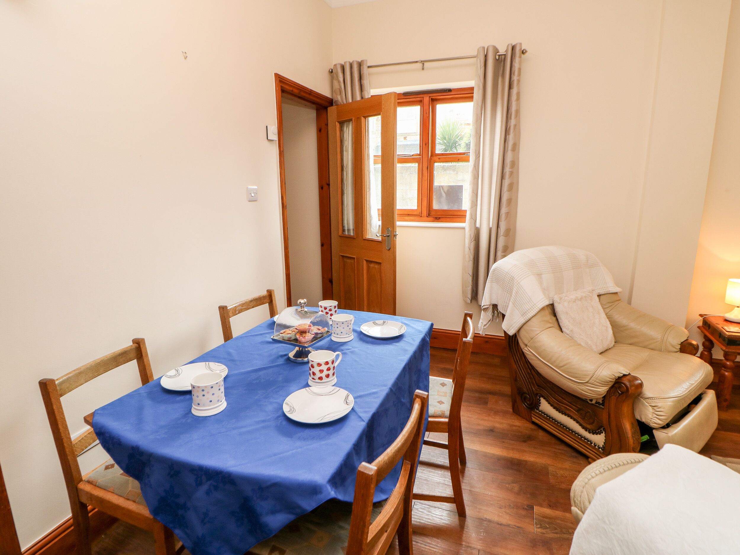 A dining area with a blue tablecloth, wooden chairs, and a window with curtains.