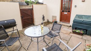 A patio with a round table, two chairs, a grill, and a barbecue grill.