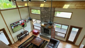 A spacious living room with a stone fireplace, leather sofa, and a television mounted on the wall. - Bourbon Country Lodge • 5 Acre Resort Pool+Hot Tub (Louisville)