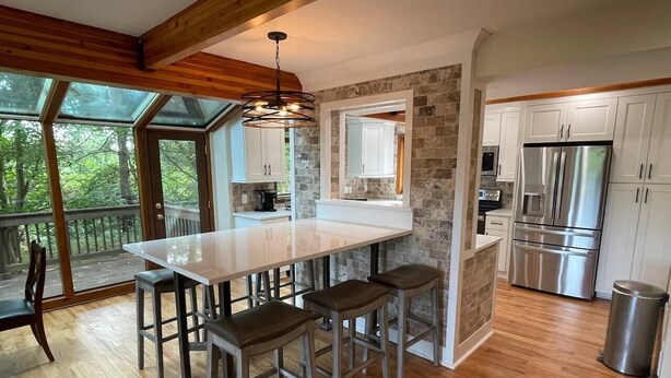 A modern kitchen with a central island, wooden flooring, and a stone accent wall. - Bourbon Country Lodge • 5 Acre Resort Pool+Hot Tub (Louisville)