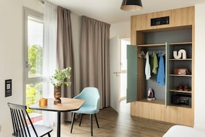 A modern room with a dining table, a chair, a plant, a wardrobe with hanging clothes, and a hanging lamp. - Appart'City Collection Saint Germain en Laye (Saint-Germain-en-Laye)