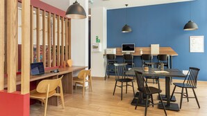 A modern office space with a long wooden partition, a desk with a laptop, multiple chairs, a table with a coffee cup, and pendant lights.