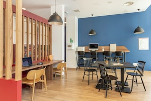 A modern office space with a long wooden partition, a desk with a laptop, multiple chairs, a table with a coffee cup, and pendant lights.
