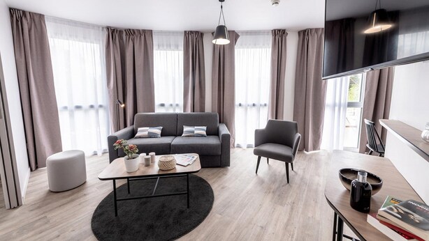 A modern living room with a grey sofa, a coffee table, and a TV. - Appart'City Collection Saint Germain en Laye (Saint-Germain-en-Laye)