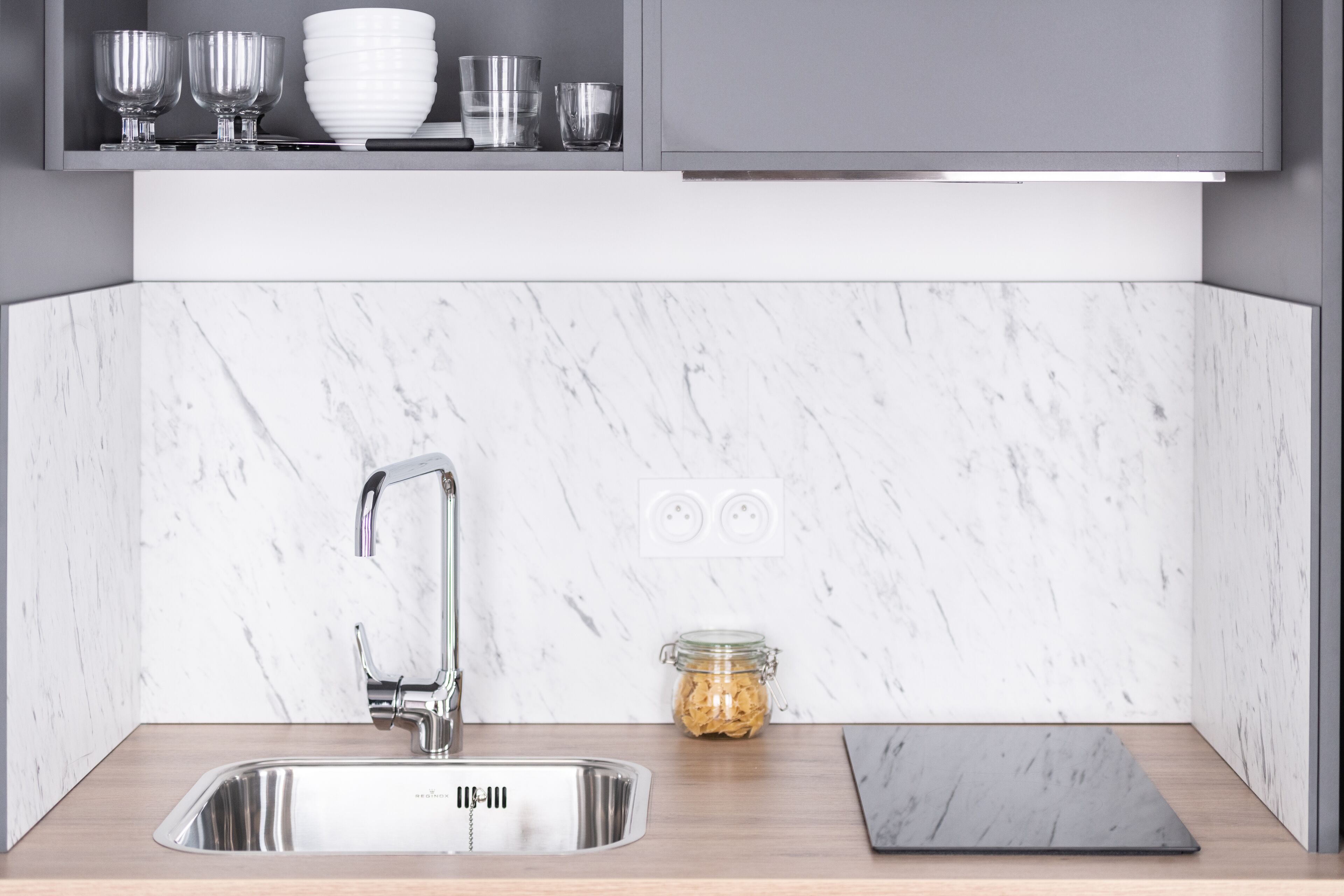 A modern kitchen with a stainless steel sink, marble backsplash, and a wooden countertop.