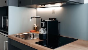 A modern kitchen with a stainless steel sink, a black coffee maker, and a built-in induction cooktop. - Appart'City Collection Saint Germain en Laye (Saint-Germain-en-Laye)