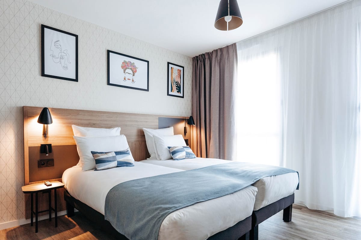 A modern hotel room with a large bed, bedside tables, and artwork on the walls.