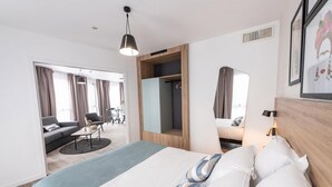 A modern hotel room with a large bed, a sofa, a dining table, and a mirror. - Appart'City Collection Saint Germain en Laye (Saint-Germain-en-Laye)