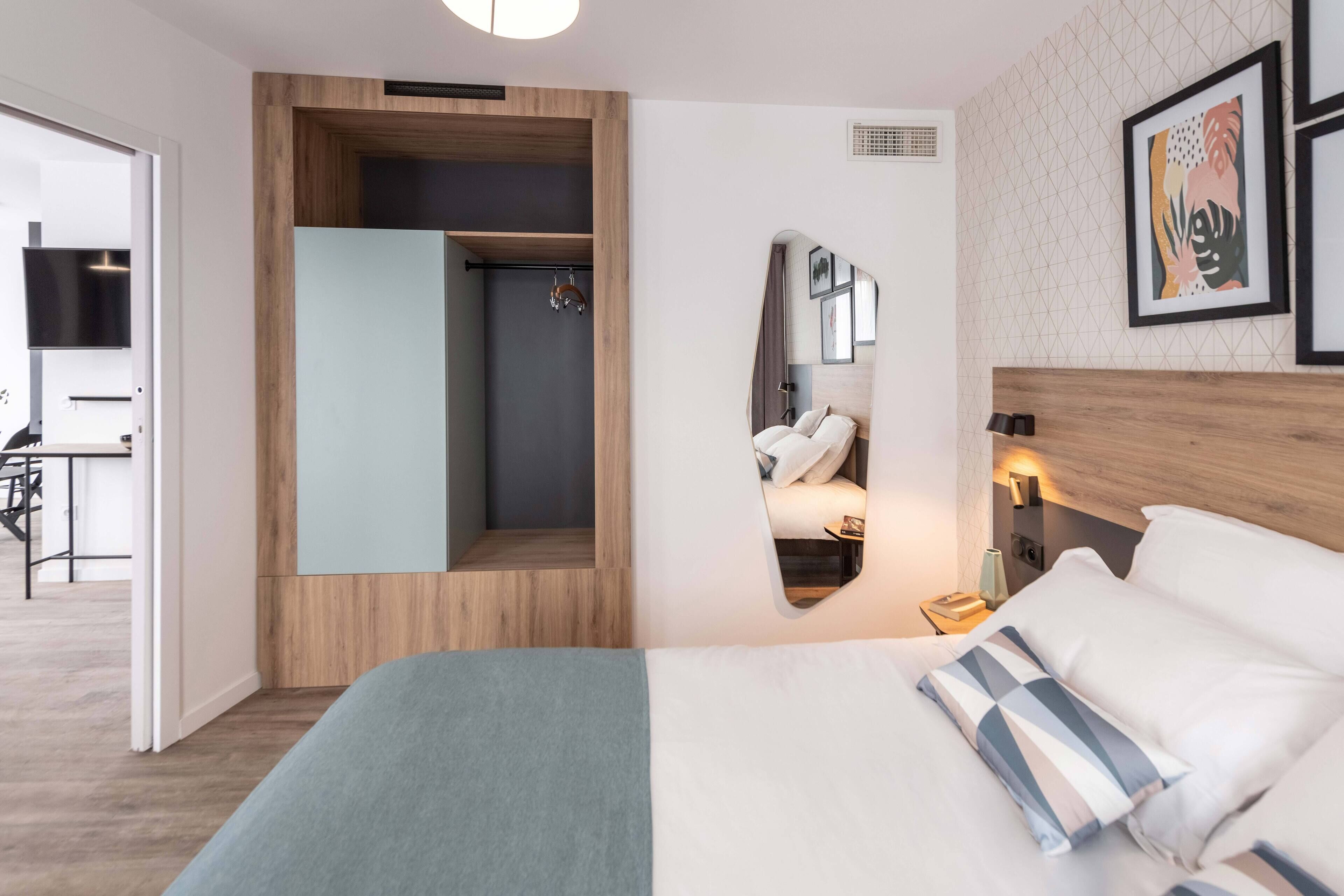 A modern hotel room with a large bed, a built-in wardrobe, a shower area, and a small seating area with a table and chairs.
