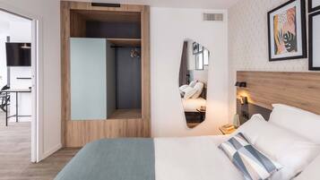 A modern hotel room with a large bed, a built-in wardrobe, a shower area, and a small seating area with a table and chairs.