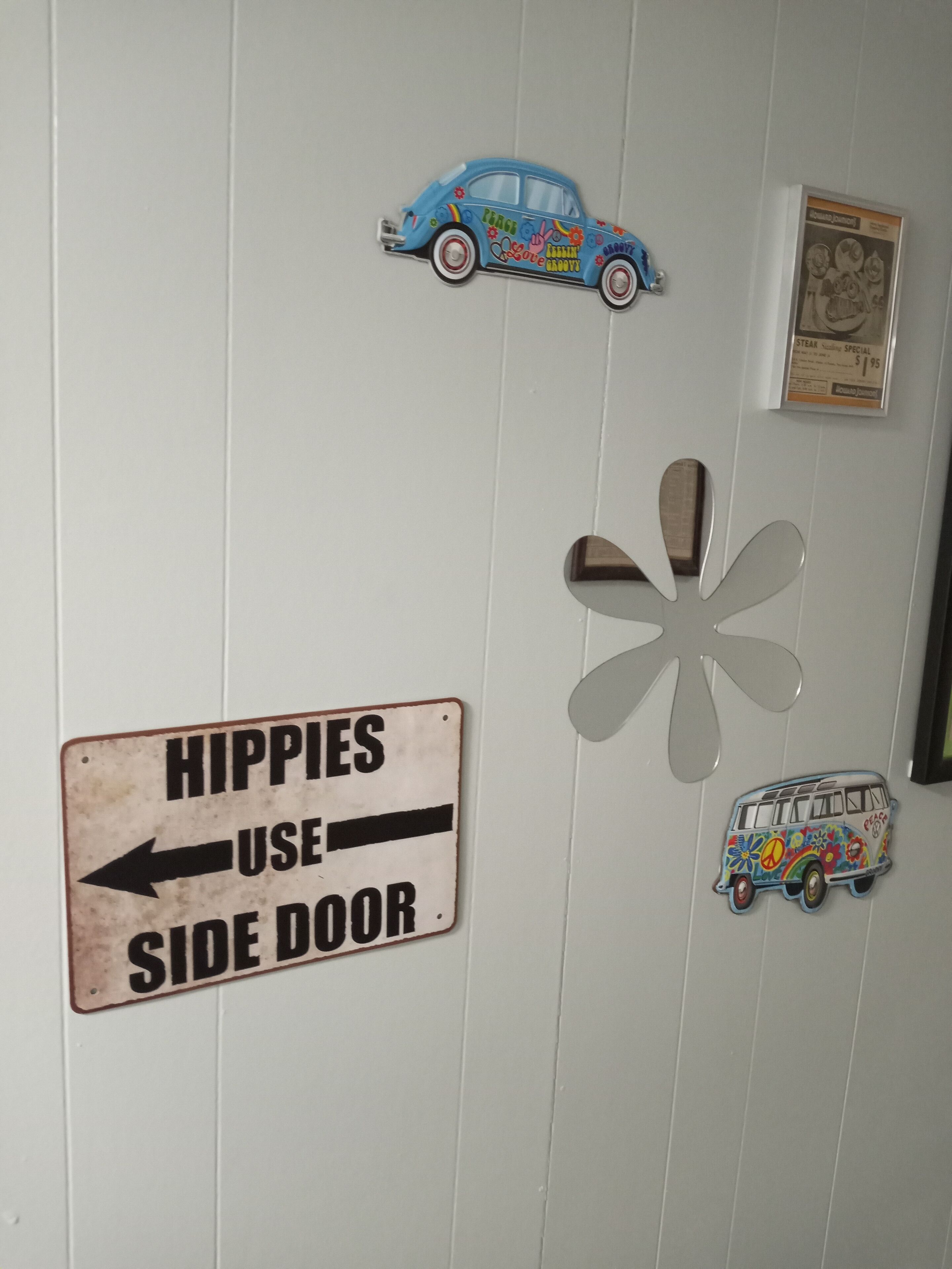 Un mur sur lequel est affiché un panneau indiquant « ENTRÉE RÉSERVÉE AUX HIPPIES », une voiture bleue et un fourgon aux motifs colorés.