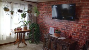 Ein gemütliches Zimmer mit Backsteinwand, Flachbildfernseher und verschiedenen Blumentöpfen.