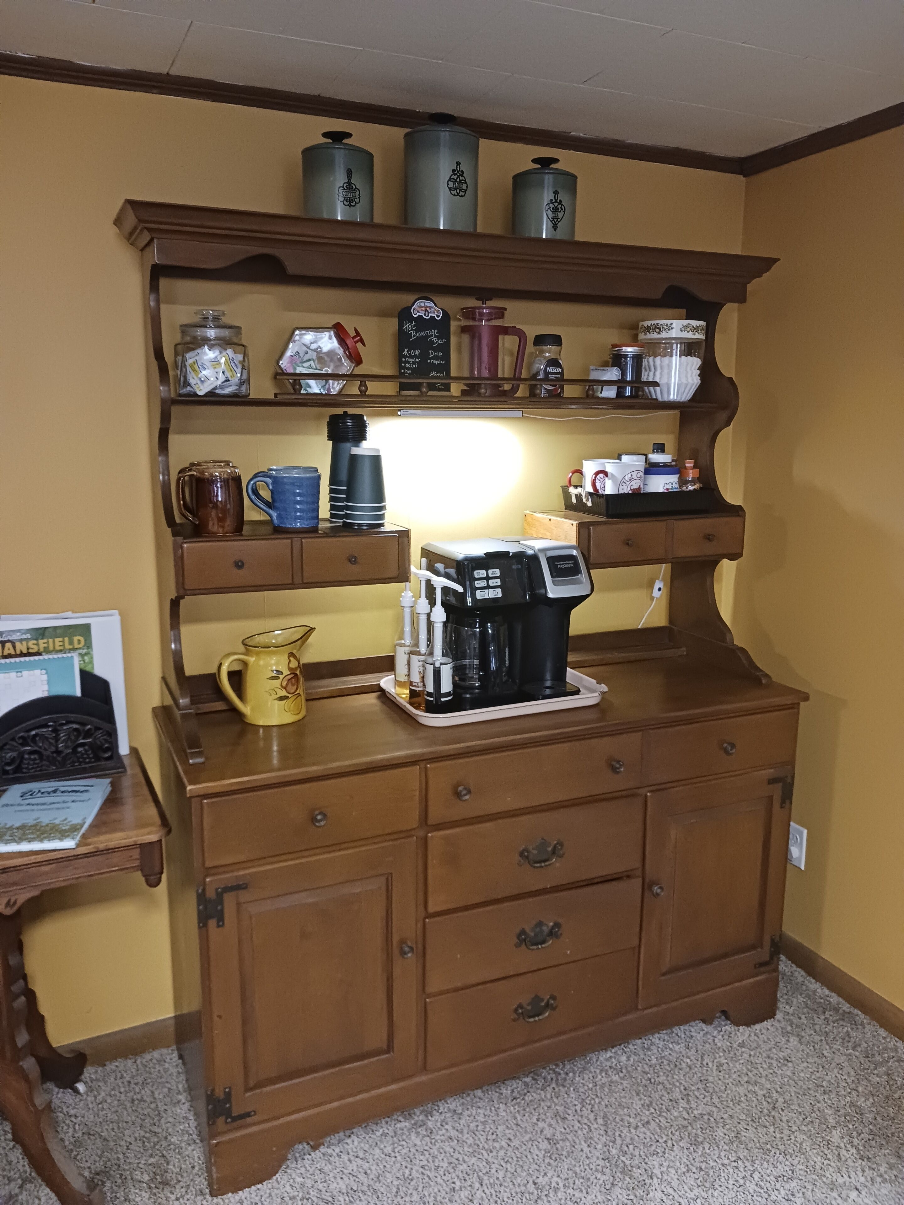 Un coin cuisine équipé d’une machine à café, de tasses et de récipients de rangement placés sur des étagères.