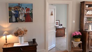 A room with a wooden dresser, a white vase with dried flowers, a lamp, a painting, and a wooden cabinet. - Le Prévôt **** Maison 1603 , Charm and luxury between Riquewihr and Ribeauvillé (Hunawihr)