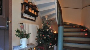 A staircase with a wooden handrail, a small bench with a potted plant, a decorated Christmas tree, and a shelf with jars and a small flag. - Le Prévôt **** Maison 1603 , Charm and luxury between Riquewihr and Ribeauvillé (Hunawihr)