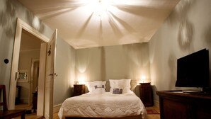 A bedroom with a large bed, bedside tables, a TV, and a wooden floor. - Le Prévôt **** Maison 1603 , Charm and luxury between Riquewihr and Ribeauvillé (Hunawihr)