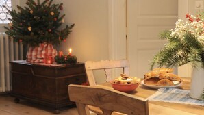 A cozy dining area with a wooden table, a chair, a Christmas tree, and a vase of flowers. - Le Prévôt **** Maison 1603 , Charm and luxury between Riquewihr and Ribeauvillé (Hunawihr)