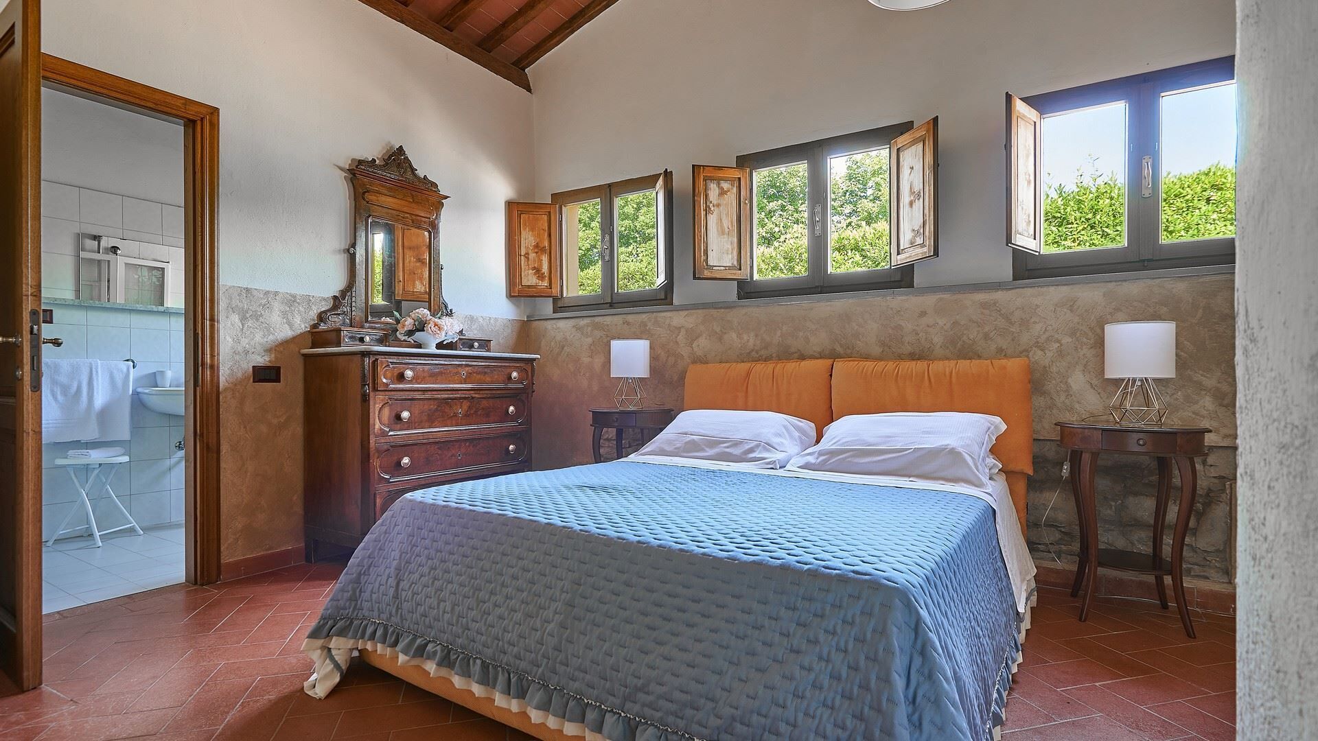 Une chambre à coucher avec un lit, une commode et une fenêtre donnant sur un paysage verdoyant.