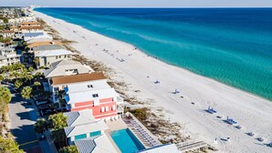 A coastal hotel with a beach view, a swimming pool, and a row of beach chairs.