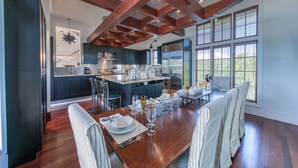 A modern kitchen with dark cabinets, a central island, and a dining area with a wooden table and striped chairs.