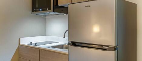 Una cocina compacta con un refrigerador de acero inoxidable, un microondas y un lavamanos.