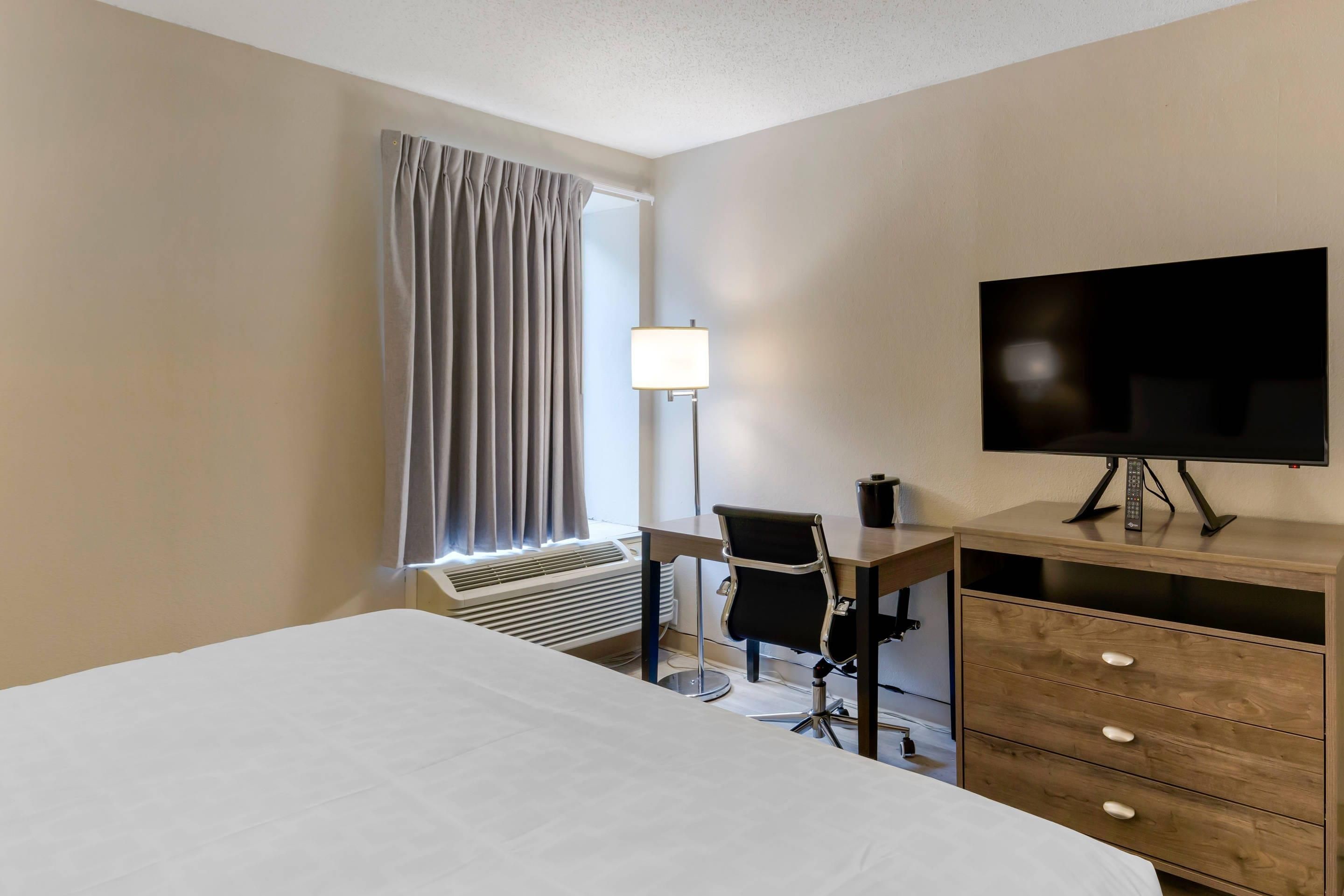 A hotel room with a bed, desk, chair, TV, and a dresser.