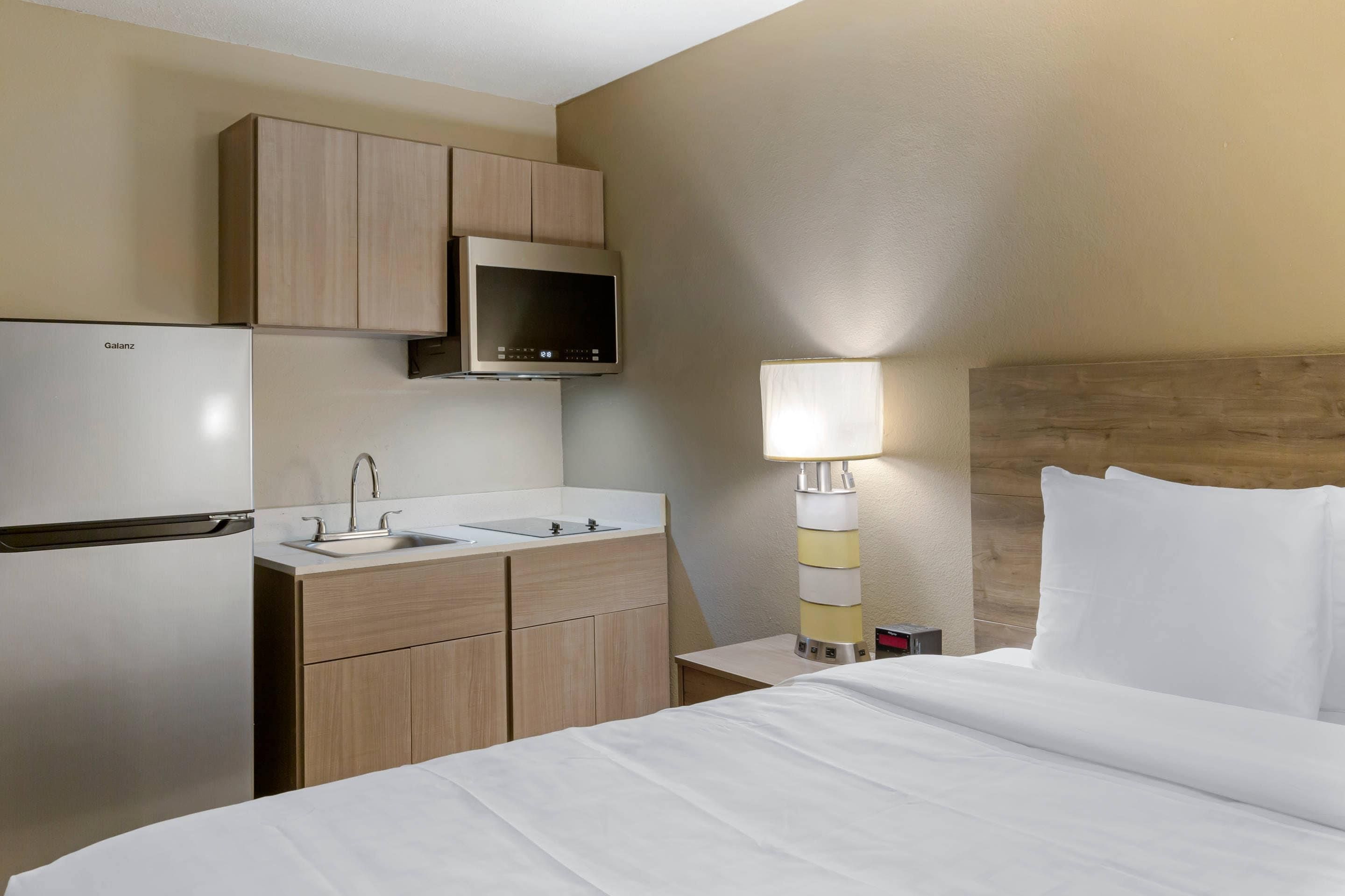 A hotel room with a bed, a bedside table with a lamp, a small desk with a sink, and a minibar.