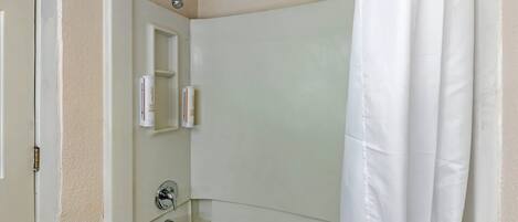 Une salle de bain avec une baignoire, un rideau de douche et une petite étagère contenant des articles de toilette.