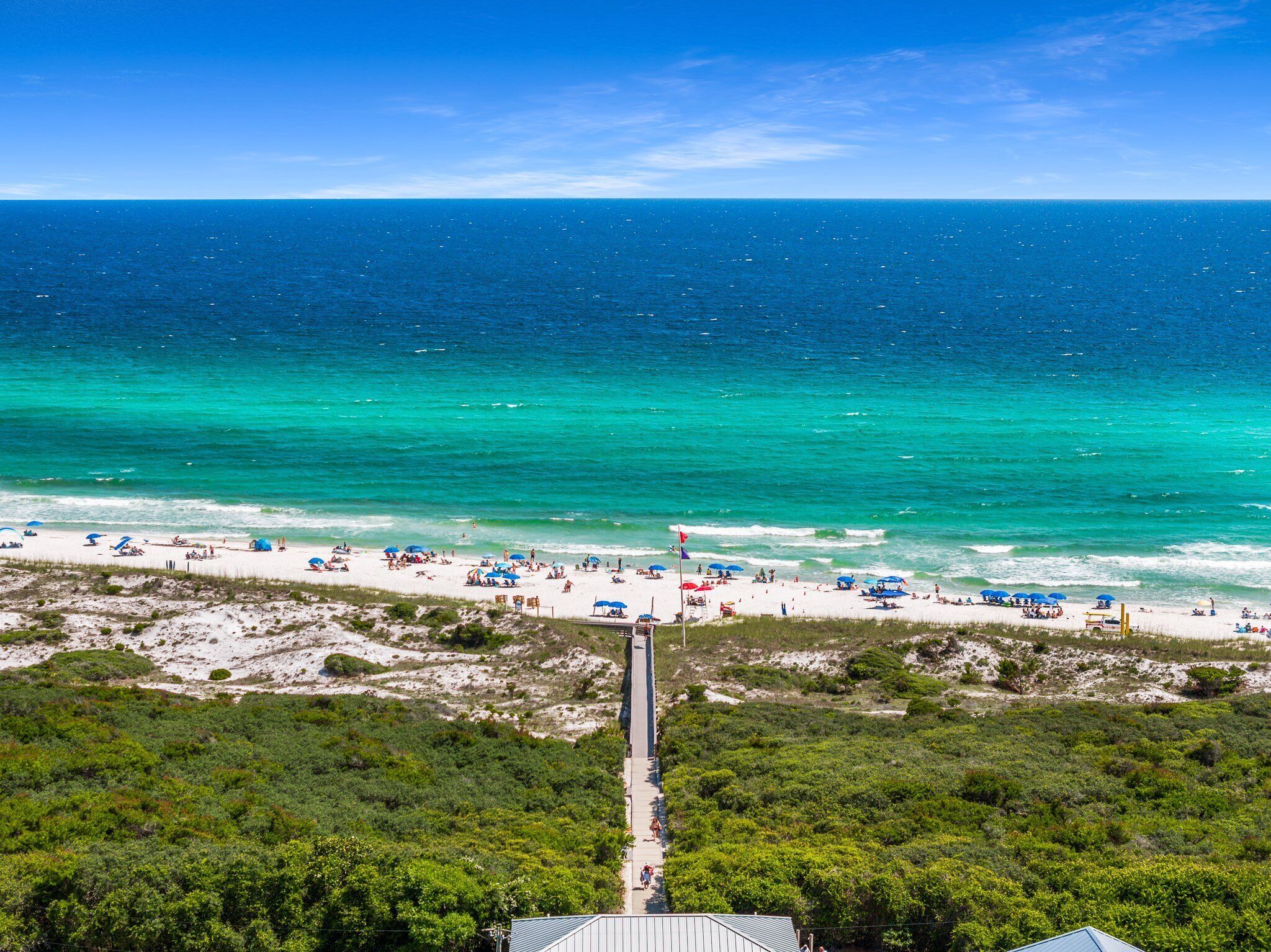 Ein Strand mit klarem türkisblauem Wasser, einem Sandstrand und einem Steg, der ins Meer führt.