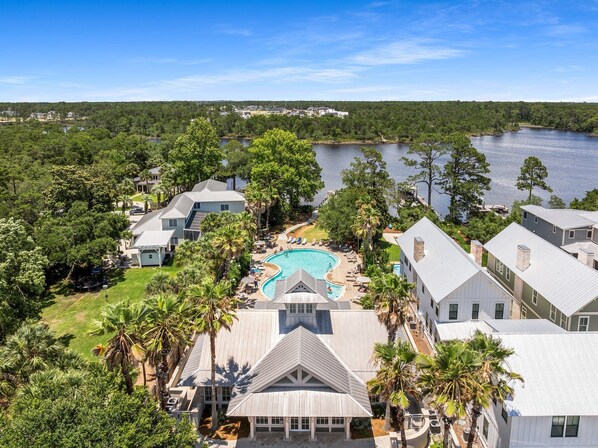 A residential area with a swimming pool surrounded by houses, trees, and a lake.
