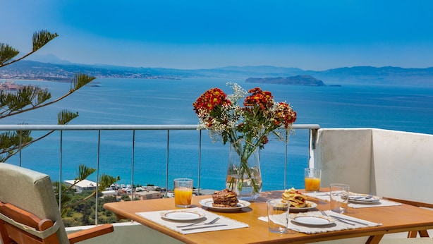 A table set for breakfast with a view of the sea, a vase with flowers, and a glass of orange juice. - Sunset Home with sea view (Chania)