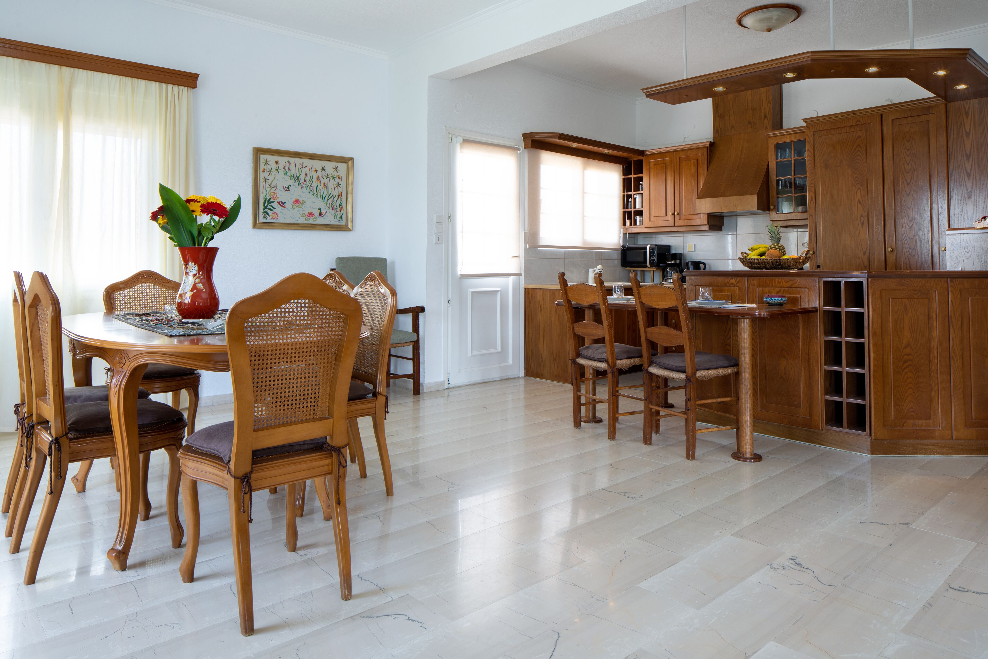 A spacious dining area with a round table and wooden chairs, a kitchen with wooden cabinets and a built-in island, and a bright, well-lit room with a large window.