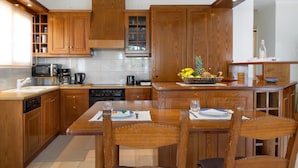 A modern kitchen with wooden cabinets, a central island, and a dining area with chairs. - Sunset Home with sea view (Chania)