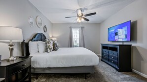 Un dormitorio con cama, ventilador de techo, televisión, cómoda y ventana con cortinas.