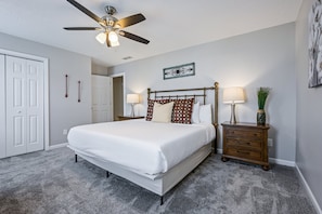 A bedroom with a bed, bedside tables, a ceiling fan, and a door.