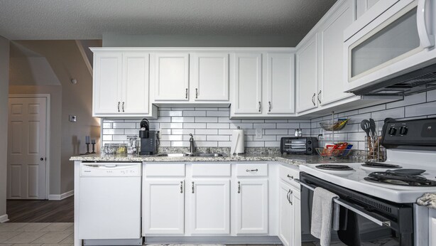 Una cocina moderna con armarios blancos, microondas integrado, estufa y lavavajillas.