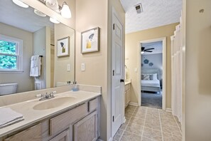 Une salle de bain avec un grand miroir, deux tableaux encadrés, un lavabo et des toilettes.