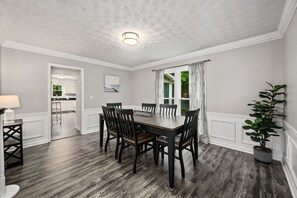 A dining area with a wooden table and chairs, a potted plant, and a view of the kitchen and dining room through a window. - Spacious 4BR in Marietta with Modern Amenities (Marietta)