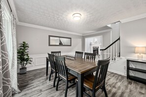Un coin repas avec une table et des chaises en bois, une plante en pot et un escalier menant à une autre pièce.