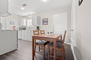 A modern kitchen with white cabinets, a dining table with chairs, and a 'THIS IS LIFE' sign on the wall.