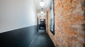 A hallway with a brick wall on one side and a plain wall on the other, leading to a door at the end.