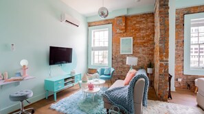 Un salon avec un téléviseur, un canapé, une table basse et un mur en briques.