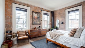 A bedroom with exposed brick walls, a wooden bed, a dresser, and a desk with a chair.