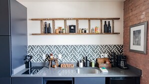 A kitchen with a modern design, featuring a black and white patterned backsplash, a wooden shelf above the counter holding various bottles and containers, and a coffee machine on the counter.
