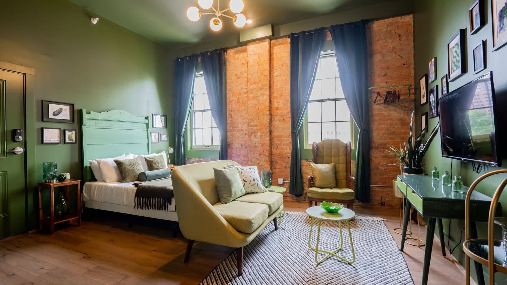 Um quarto com cama, sofá, poltrona, televisão e parede de tijolos.