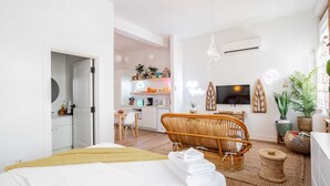Et moderne hotelværelse med en seng, en fletstol, et lille bord og et tekøkken i baggrunden.