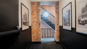 A hallway with a brick wall, a staircase, and framed pictures on the walls.