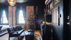 Una habitación con pared de ladrillo, chimenea, estantería, sofá de cuero y televisor.