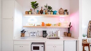 A modern kitchen with white cabinets, a microwave, a coffee maker, and a neon sign that reads "Welcome to Neon."
