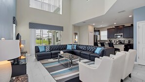 Ein geräumiges Wohnzimmer mit einer Eckcouch, einem Couchtisch und einem Essbereich mit weißen Stühlen. Im Hintergrund ist eine Küche zu sehen.